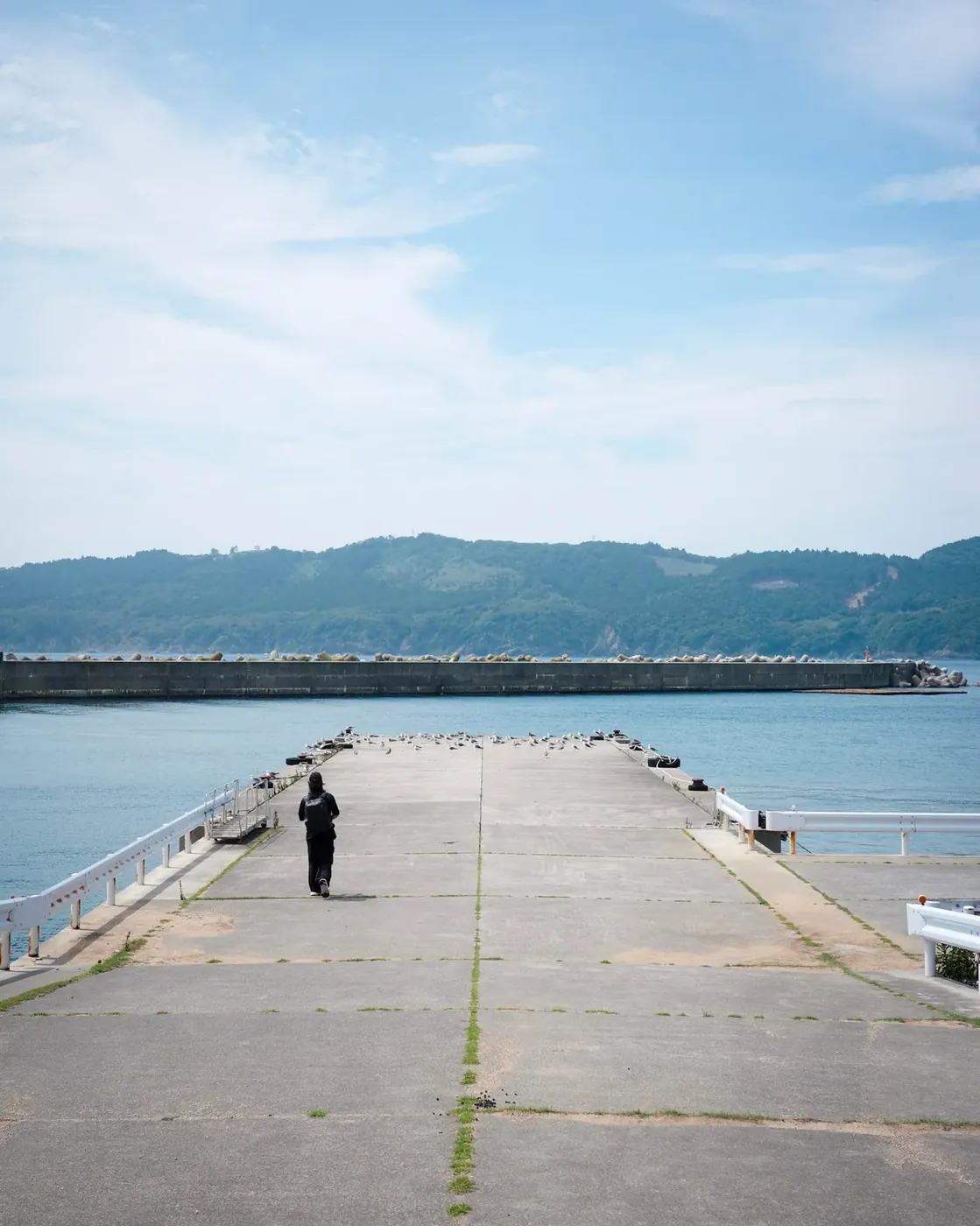 青空の下、海へ伸びる桟橋を歩く人