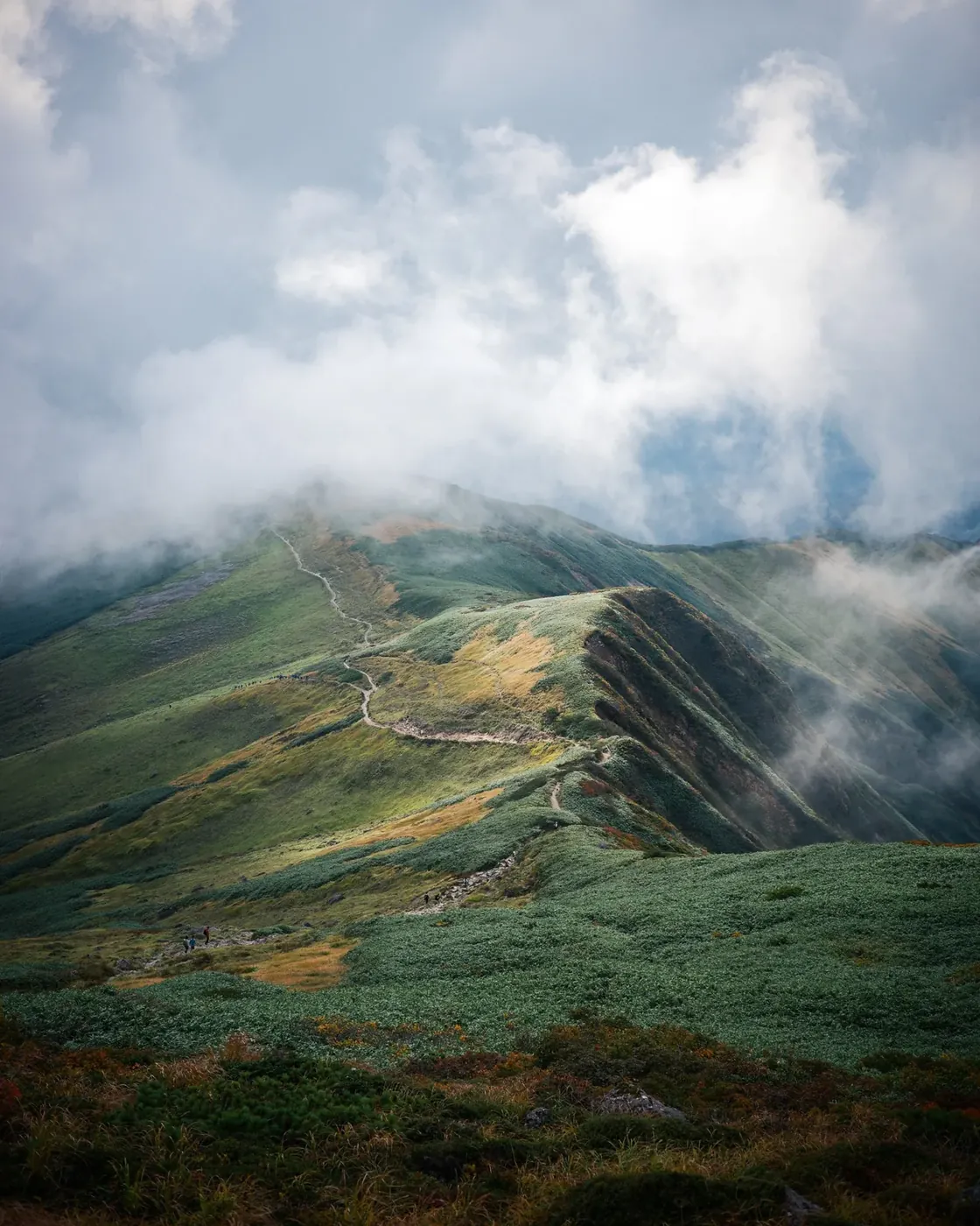 雲が流れる緑の稜線と登山道