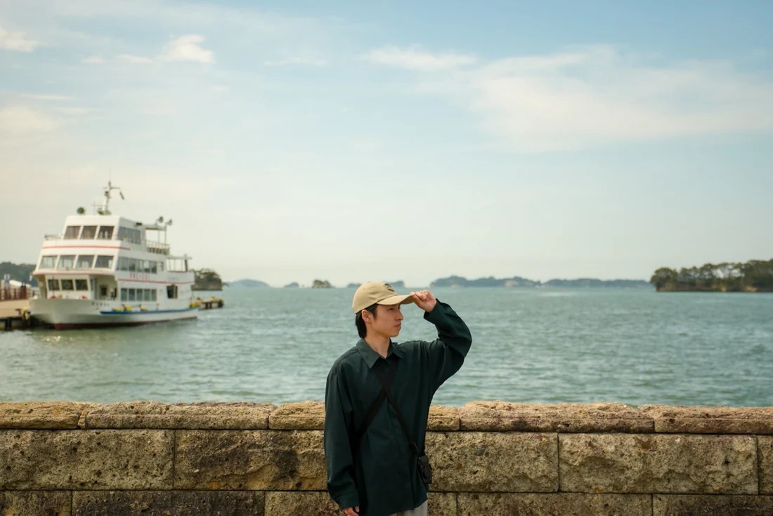 松島の海を背景に、BULLETISの帽子をかぶるTANAYAN